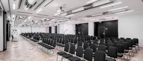 Una sala de conferencias con filas de sillas, un escenario y una puerta negra grande.