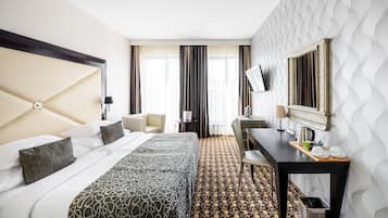 A hotel room with a large bed, a desk, a chair, a TV, and a patterned carpet.