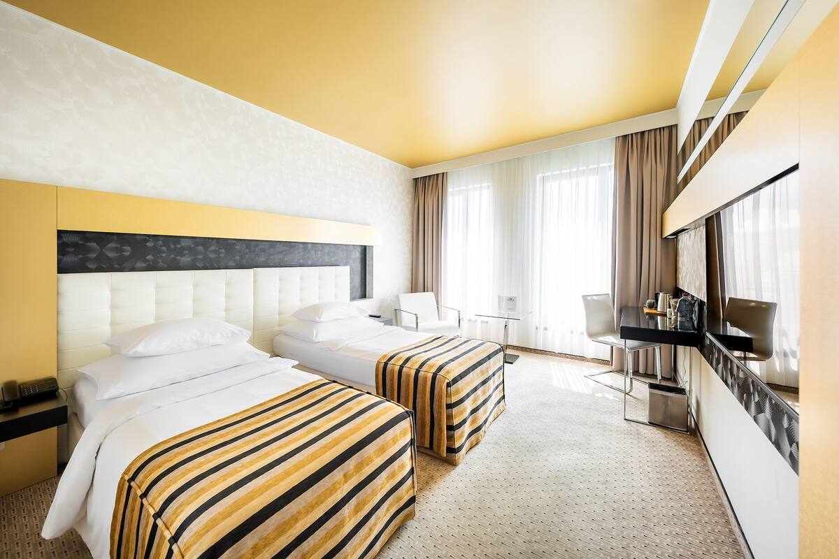 A hotel room with two beds, a desk, a chair, and a TV.