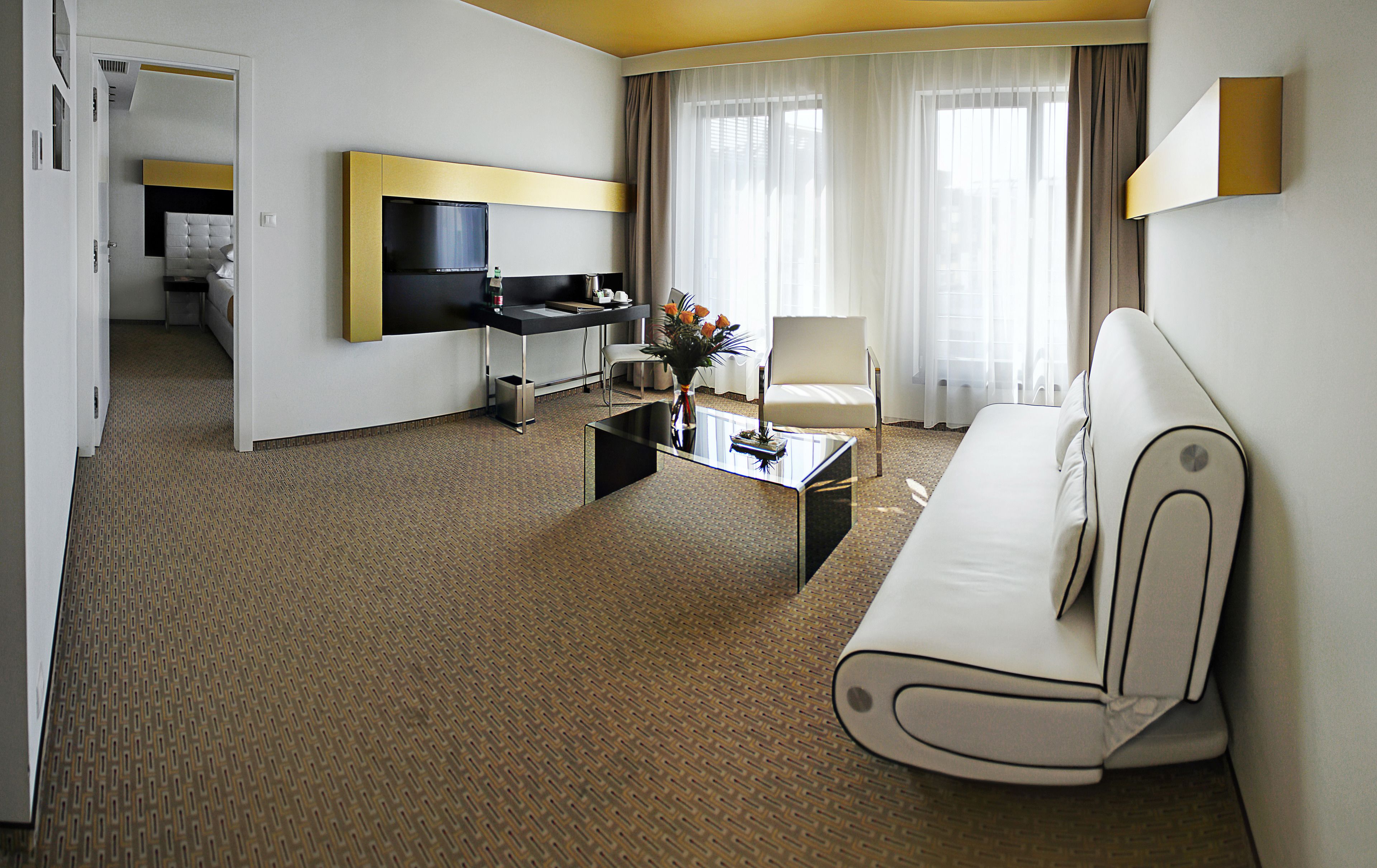 A hotel room with a sofa, a coffee table with a vase of flowers, a television, and a desk with a chair.