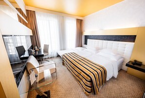Um quarto de hotel com uma cama, uma escrivaninha com cadeira, uma mesinha de vidro e um telefone.