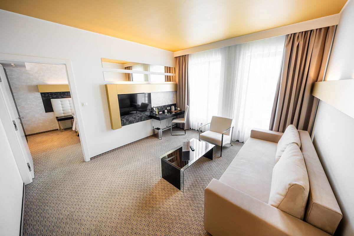 A modern hotel room with a sofa, a coffee table, a TV, and a dining area.