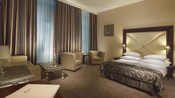 A hotel room with a large bed, two armchairs, a small table, and a desk with a lamp.