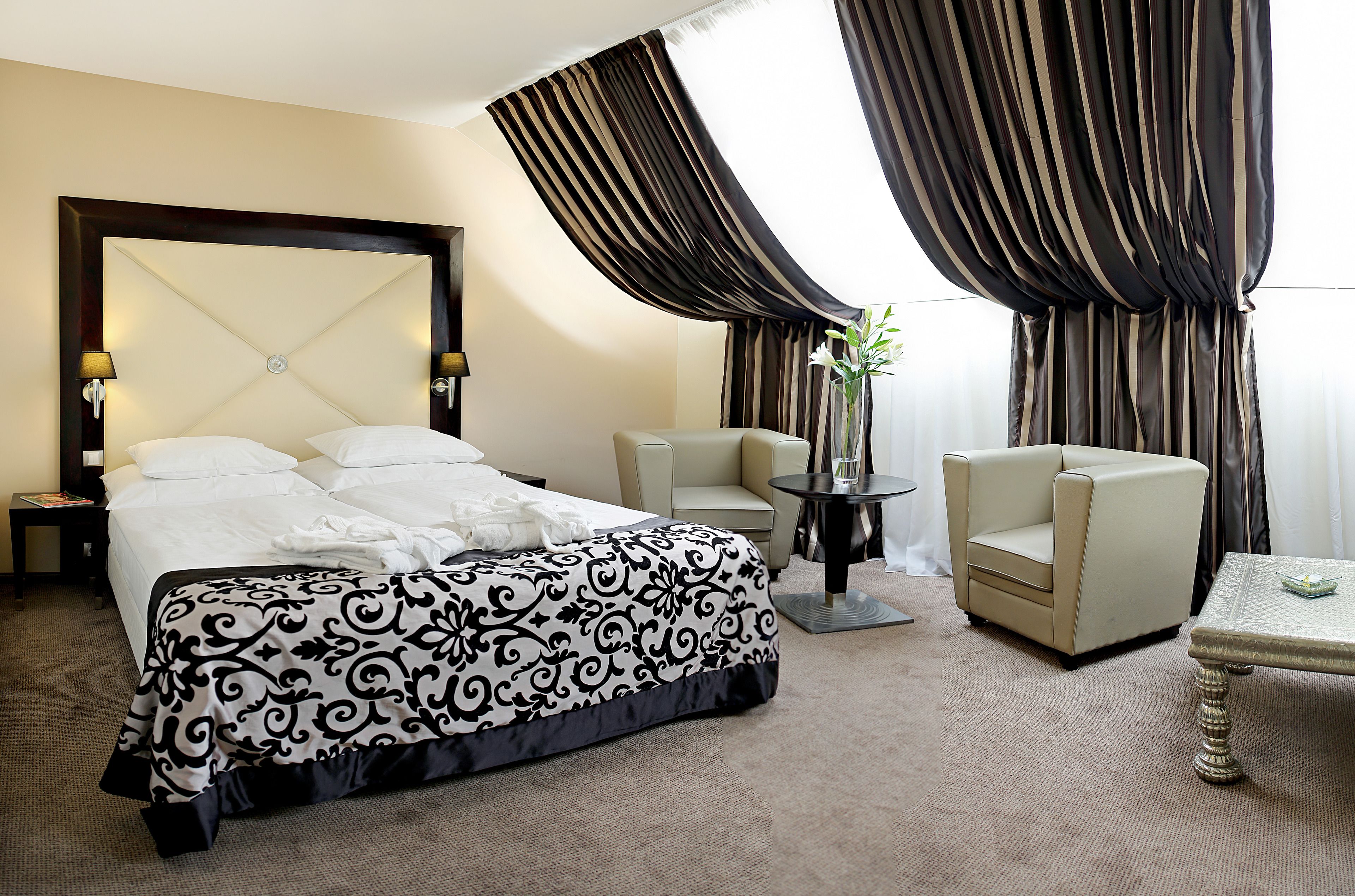 Una habitación de hotel con una cama grande, dos sillas, una mesita y un jarrón con flores.