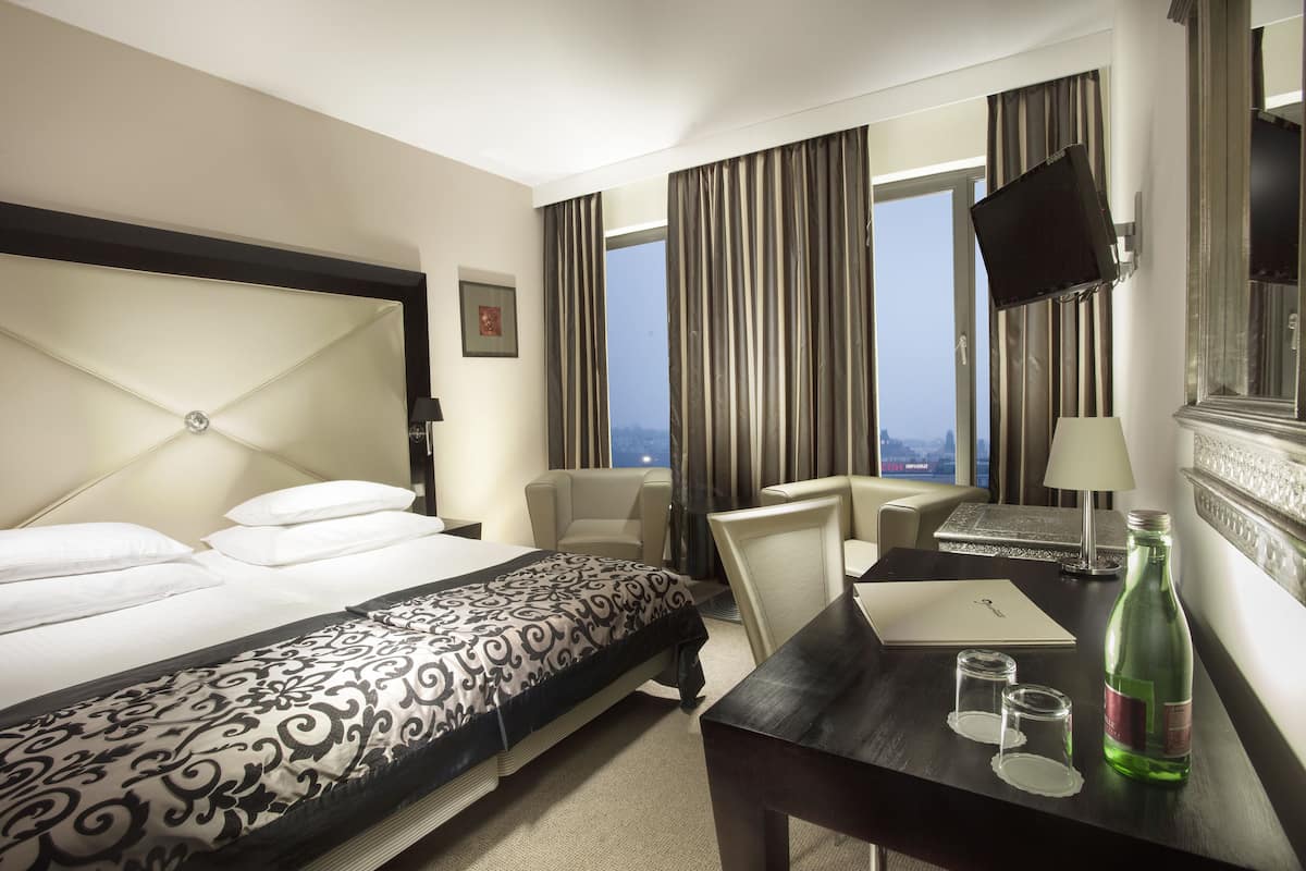 A hotel room with a bed, a desk, a chair, a television, and a window with curtains.