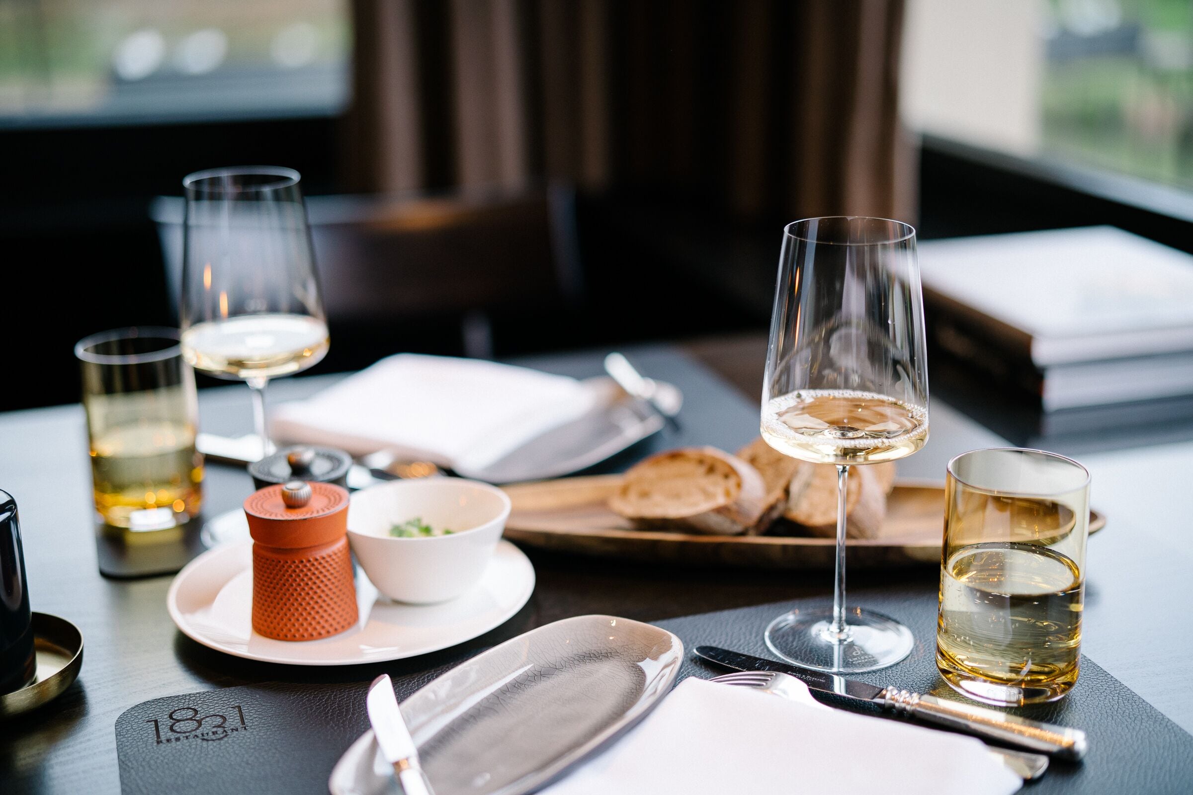 Una mesa de comedor dispuesta con copas de vino, platos y una cesta de pan.