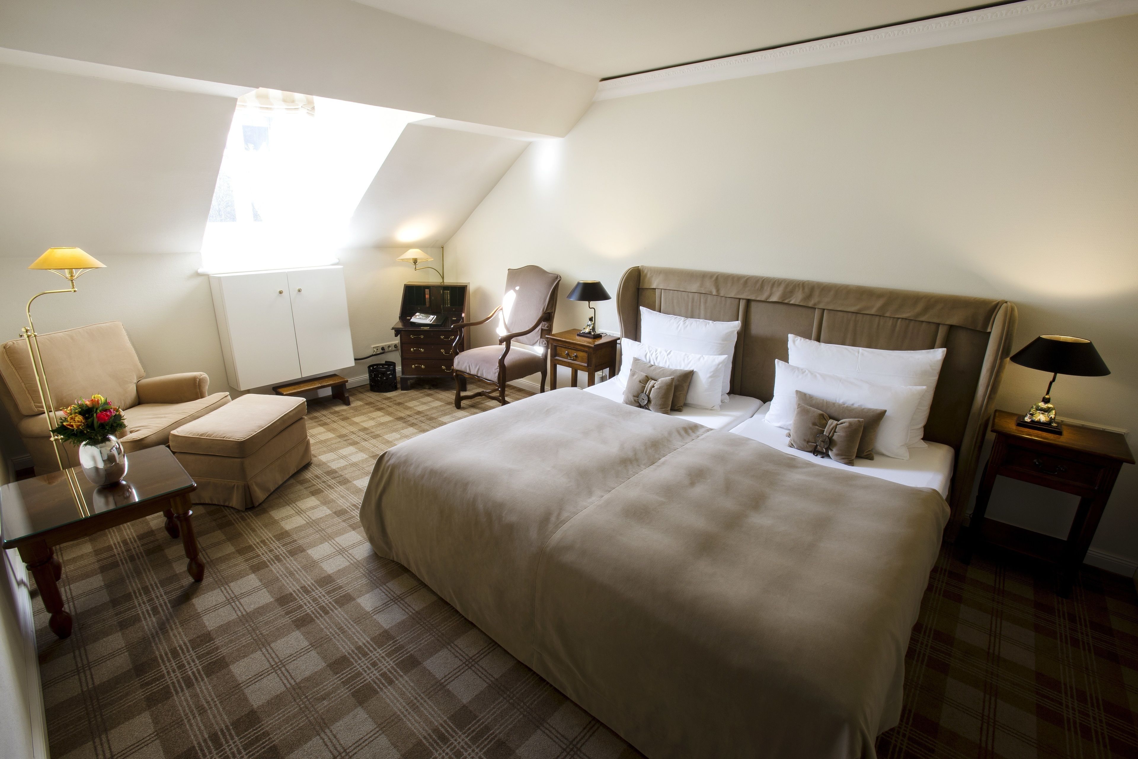 Hotelkamer met een groot bed, een bureau, een stoel en een klein tafeltje. Een raam zorgt voor natuurlijk licht.