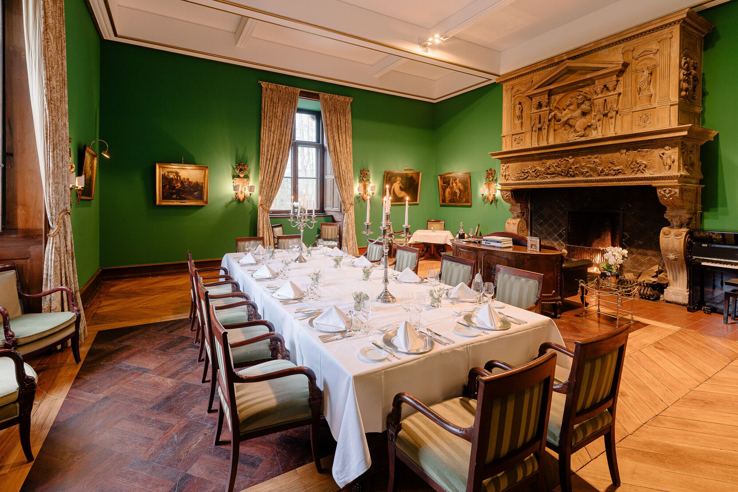 A formal dining room with a long table set for a meal, green walls, and a fireplace with intricate carvings.