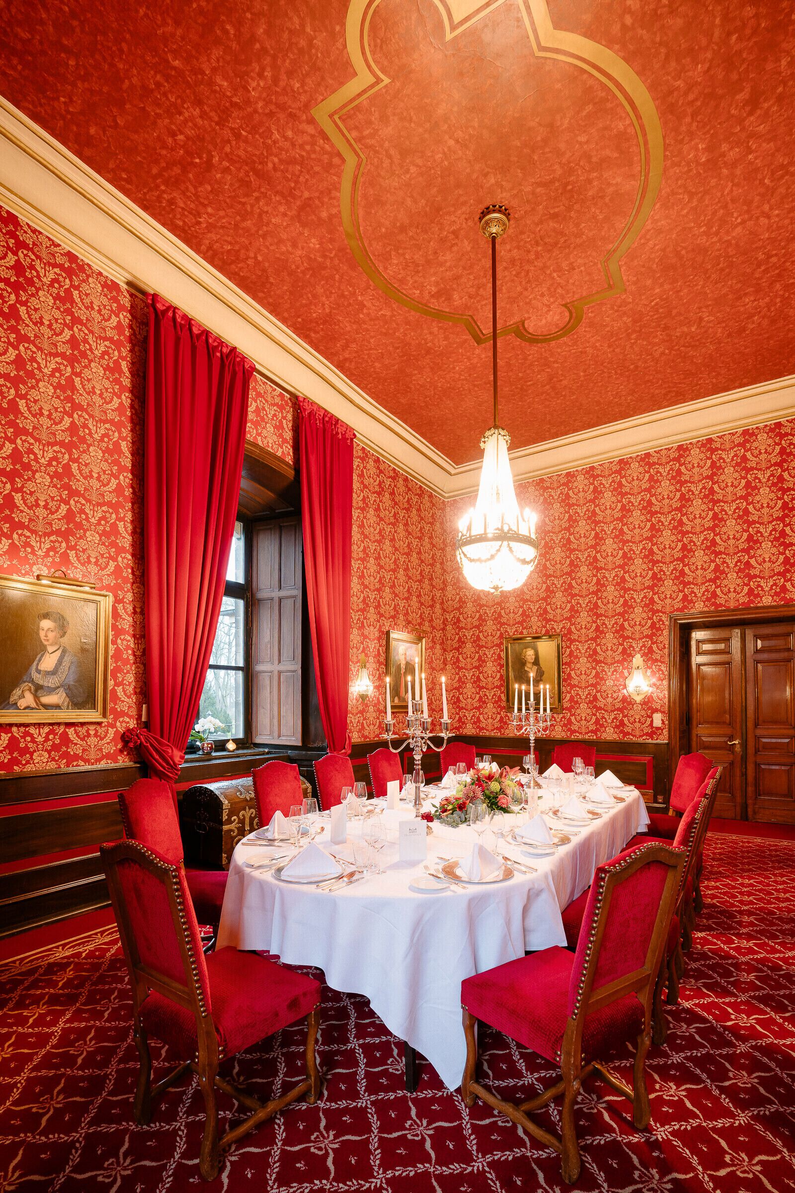 Ein formeller Speisesaal mit einem runden Tisch, gedeckt für sechs Personen, roten Stühlen und einer Kristallleuchter.