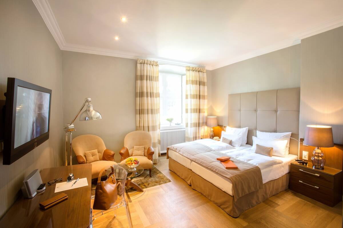 Een hotelkamer met een bed, nachtkastjes, een bureau, een stoel, een lamp en een raam met gordijnen.
