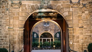 Ein steiner Torbogen führt zu einem Innenhof mit einem Ziegeldach und einem kleinen Fenster darüber.