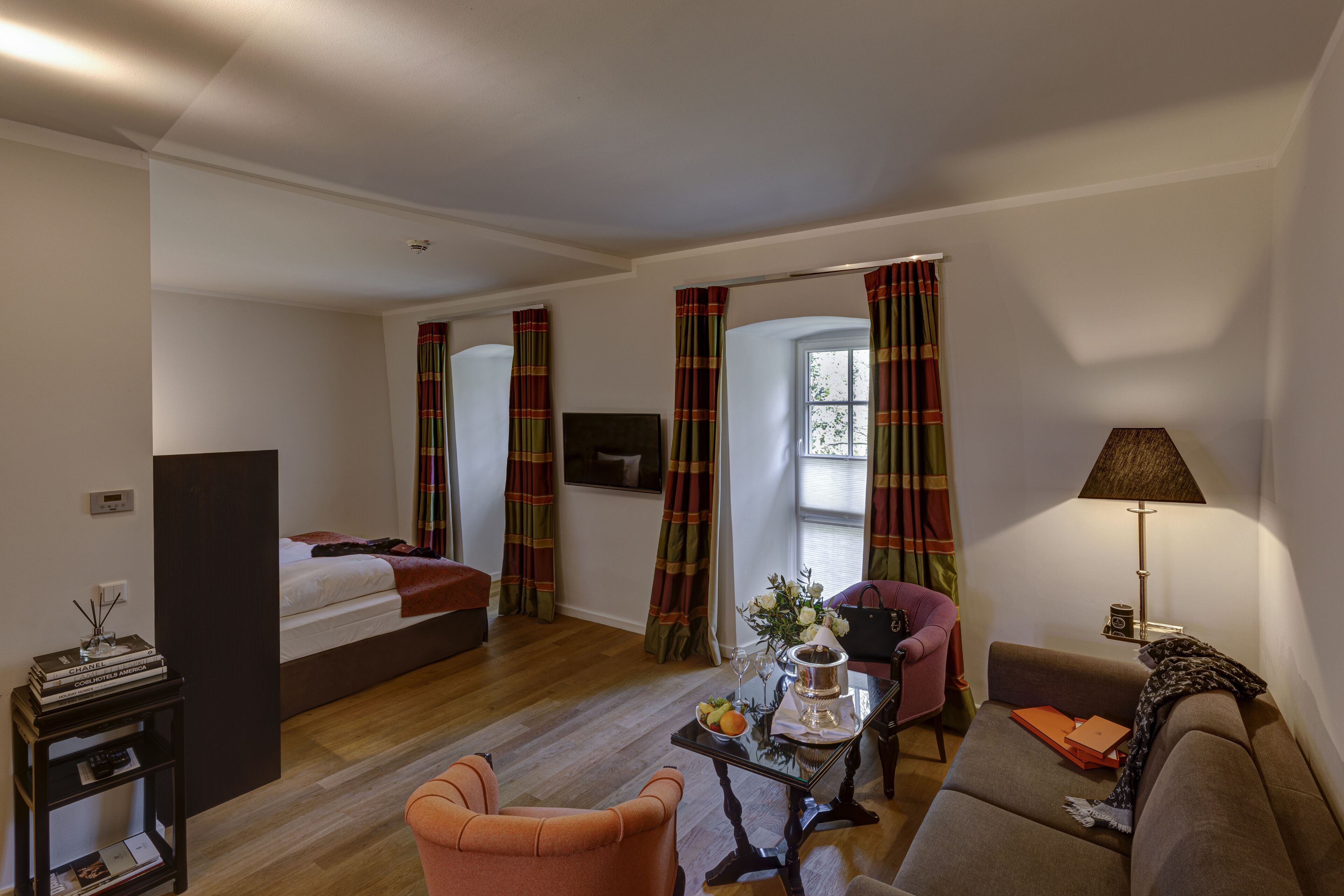 Une chambre d’hôtel moderne comprenant un lit, deux coins salon, une petite table avec un vase et une lampe.