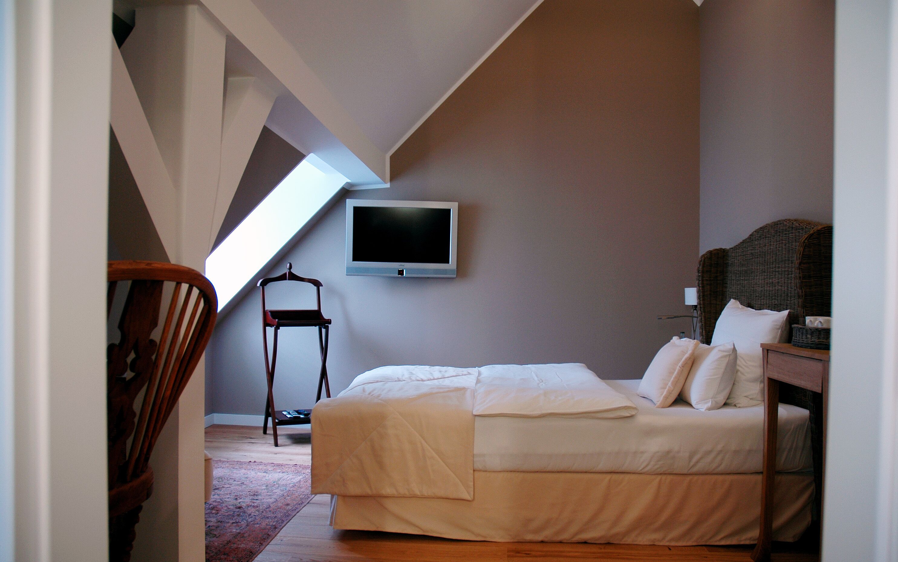 A bedroom with a bed, a chair, a television, and a view of the sky.