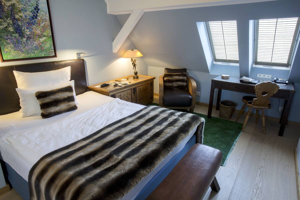 Een hotelkamer met een groot bed, een bureau, een stoel en een raam met jaloezieën.
