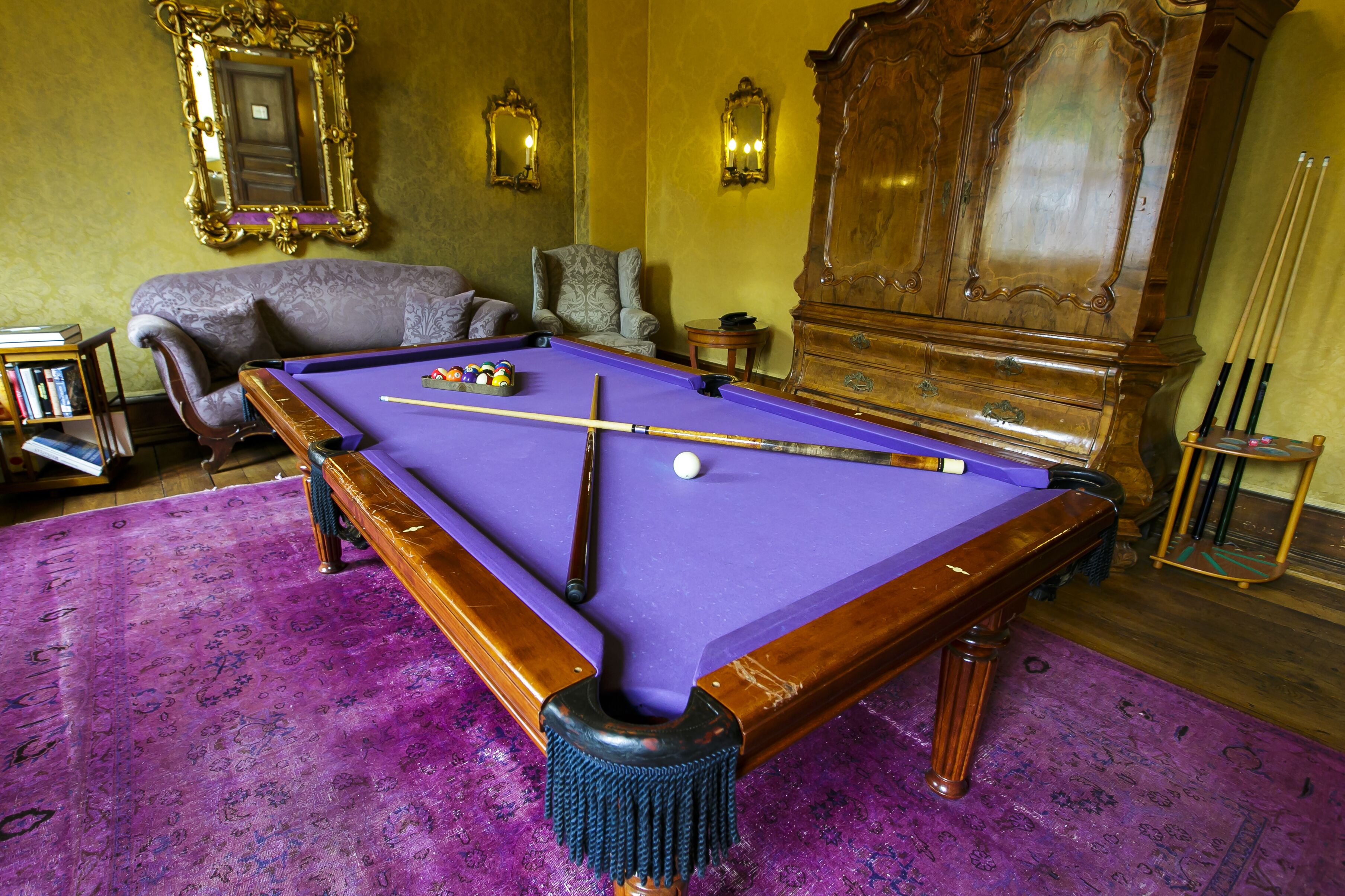 Uma mesa de bilhar com superfície em feltro roxo, rodeada por um tapete roxo.
