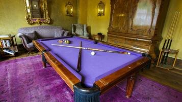 Uma mesa de bilhar com superfície em feltro roxo, rodeada por um tapete roxo.