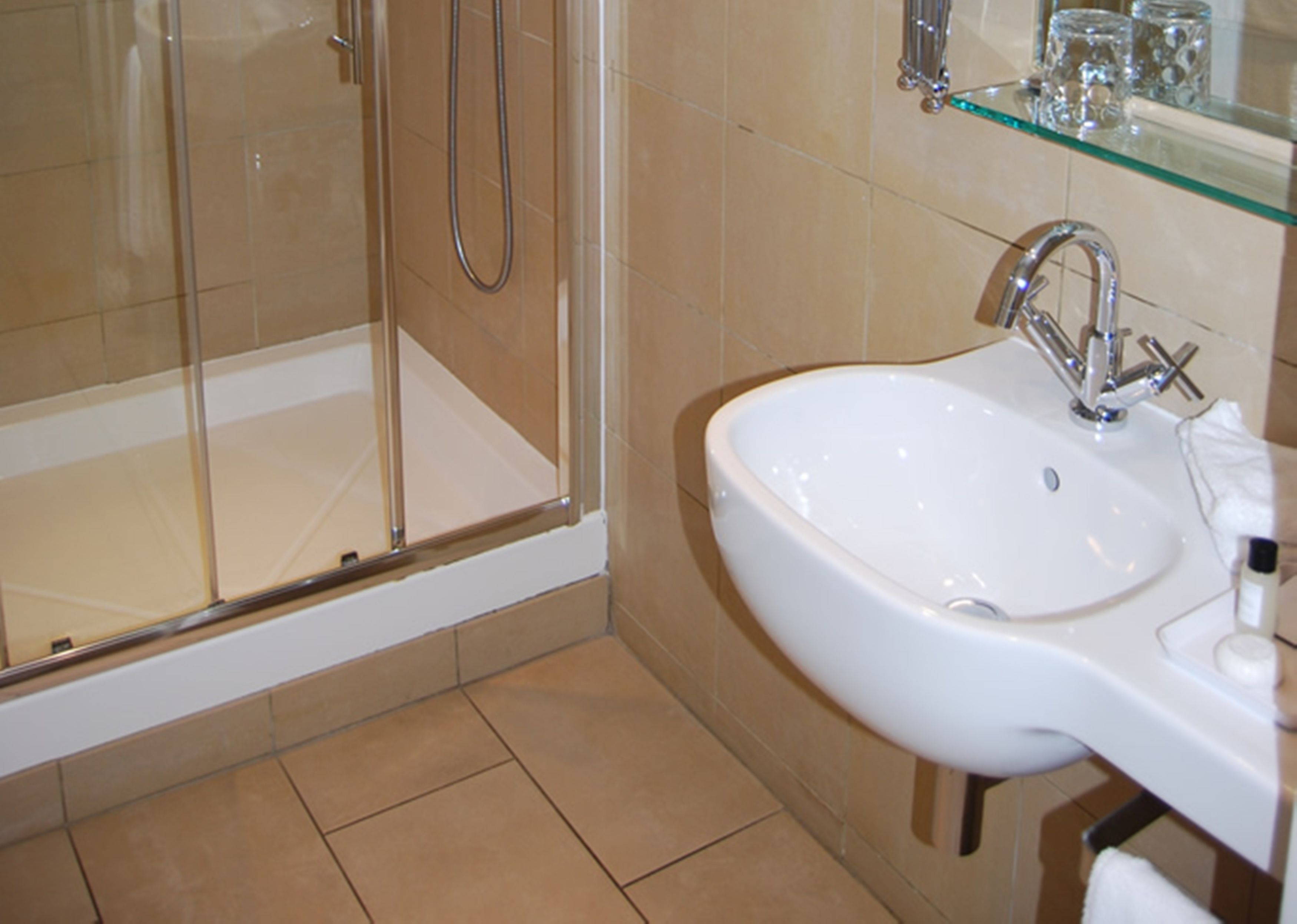 A bathroom with a glass-enclosed shower, a white sink with a modern faucet, and a glass shelf above the sink.