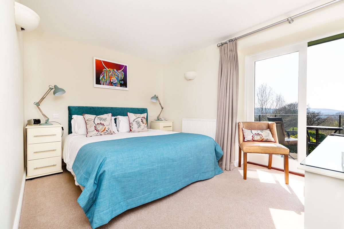 A bedroom with a bed, two bedside lamps, a chair, a window, and a radiator.