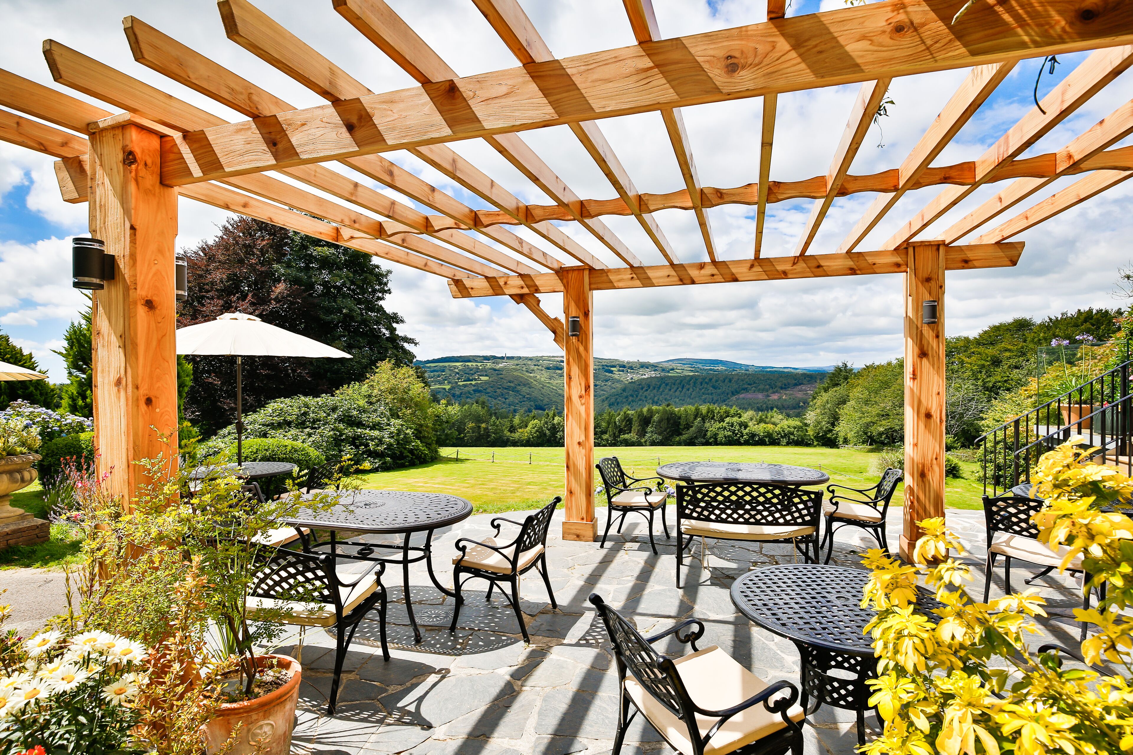An outdoor patio with wooden pergola, stone flooring, and tables with chairs.