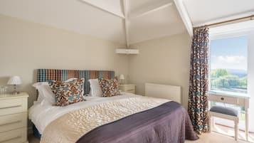 Un dormitorio con una cama grande, una mesita de noche con lámpara, una ventana con cortinas y vistas al exterior.
