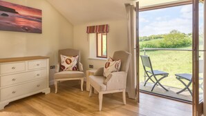 A room with two armchairs, a wooden dresser, a window with a view of the outdoors, and a door leading to an outdoor seating area. - The Horn of Plenty (Tavistock)