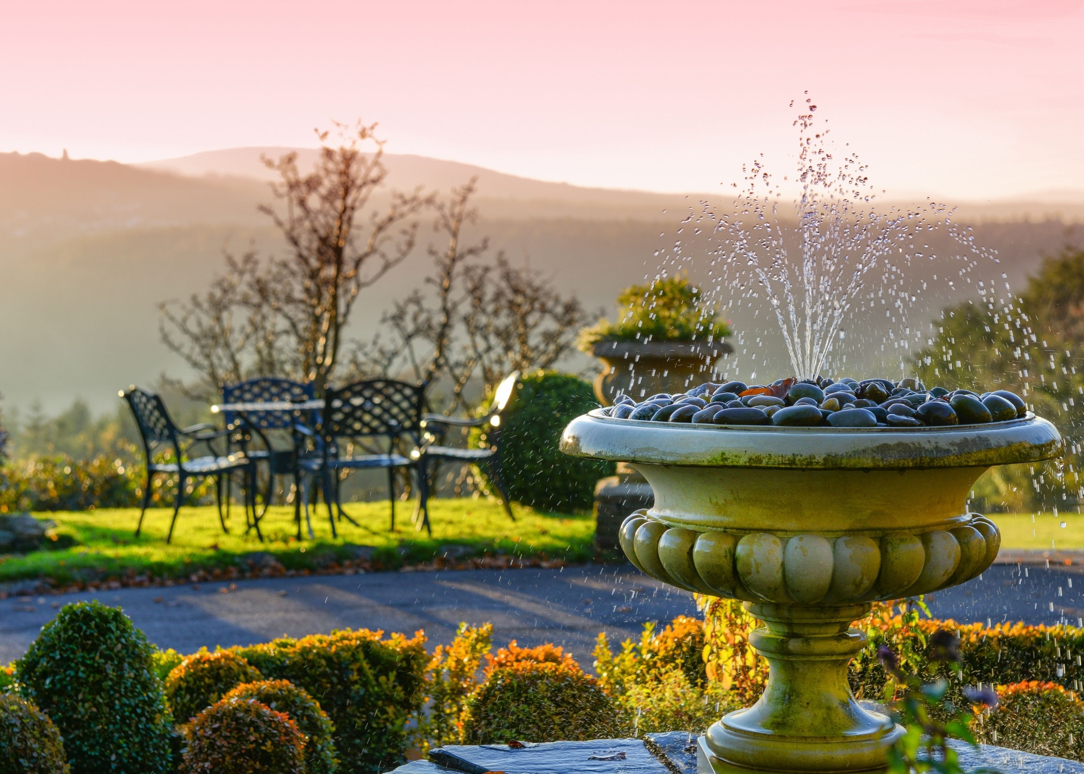 A garden with a fountain, a bench, and a table.