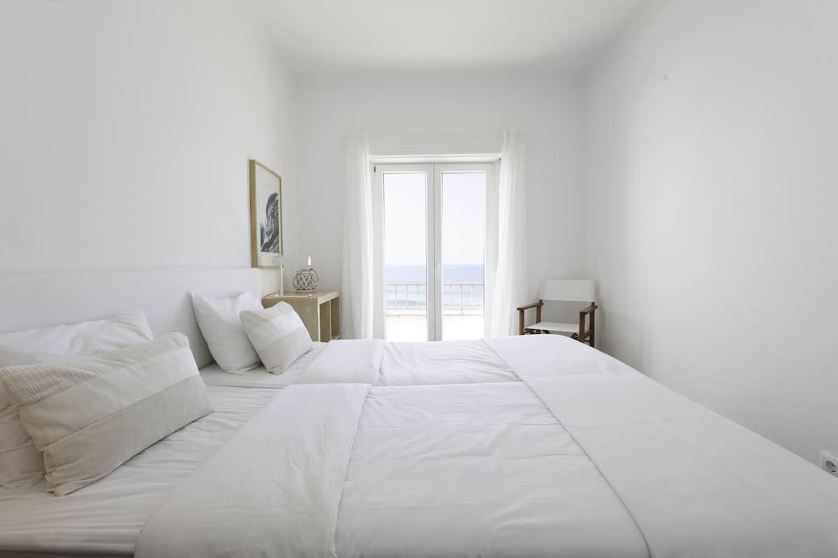 Een slaapkamer met een groot bed, een nachtkastje, een stoel en een raam met uitzicht.