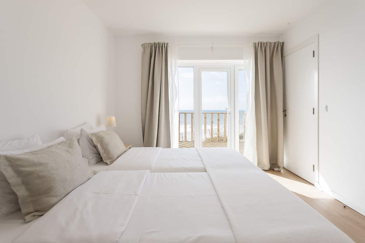 Een slaapkamer met een groot bed, een nachtkastje en uitzicht op het strand door een glazen deur.