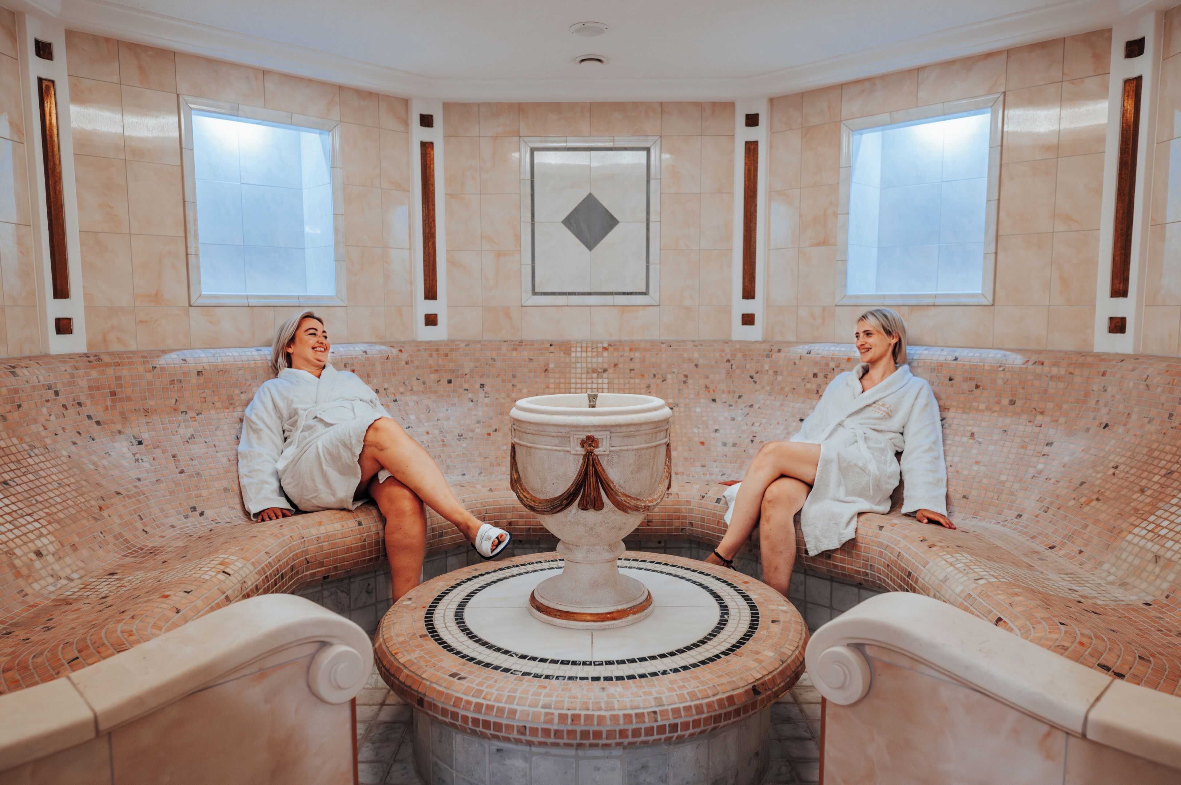 Two people sitting on a spa bench with a decorative fountain in the center.