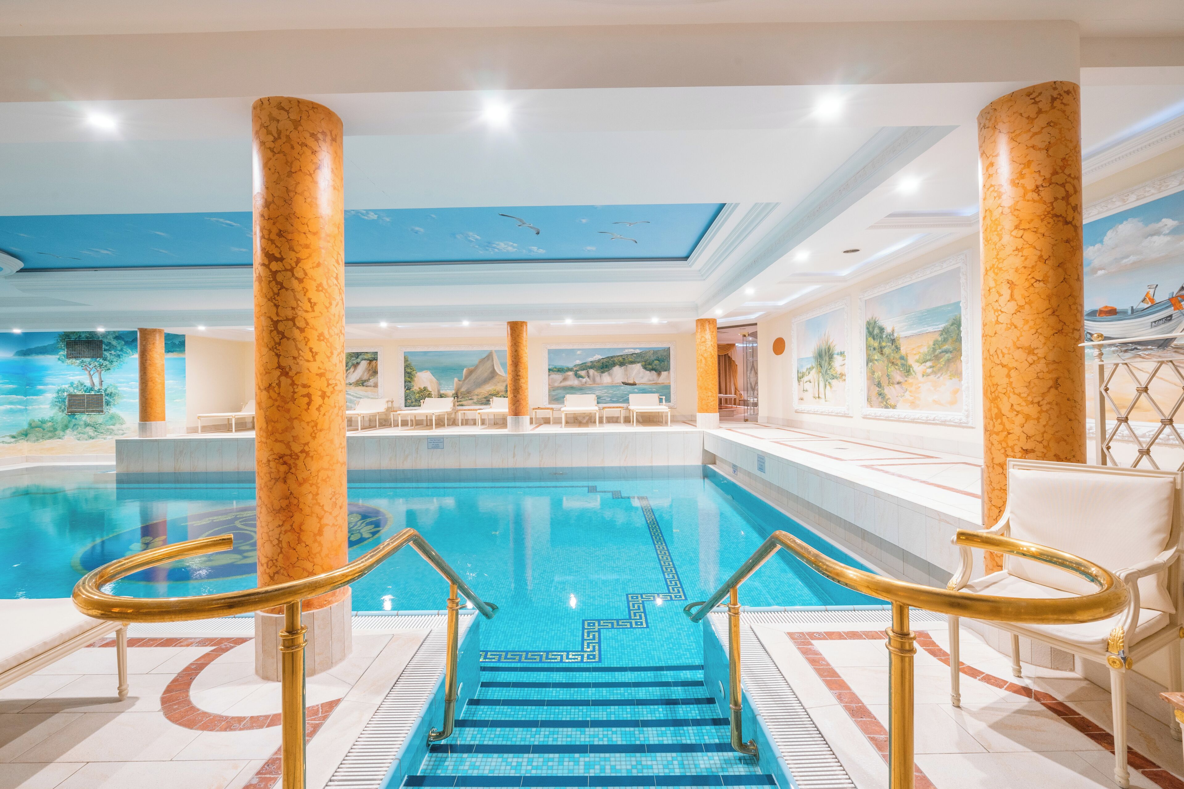 Une piscine intérieure ornée de colonnes en marbre, dotée d’un sol carrelé et d’une fresque murale au plafond.