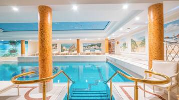 Une piscine intérieure ornée de colonnes en marbre, dotée d’un sol carrelé et d’une fresque murale au plafond.