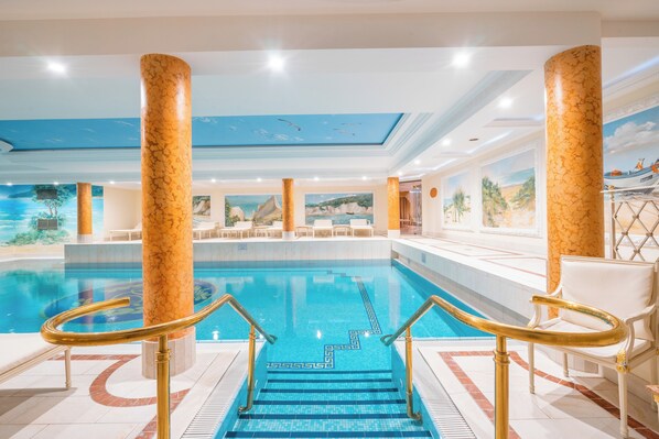 Une piscine intérieure ornée de colonnes en marbre, dotée d’un sol carrelé et d’une fresque murale au plafond.