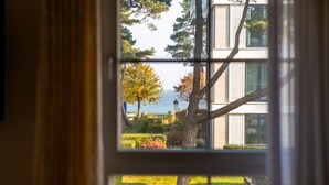 A window view of a building with a clear sky, a tree with autumn leaves, and a distant view of the sea. - Strandresidenzen Binz (Binz)