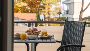 A table with breakfast items including bread, fruit, and juice, set on a balcony with a view of trees and buildings. - Strandresidenzen Binz (Binz)