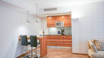 A modern kitchen with wooden cabinets, a microwave, and a coffee maker. There is a dining area with two chairs and a table.
