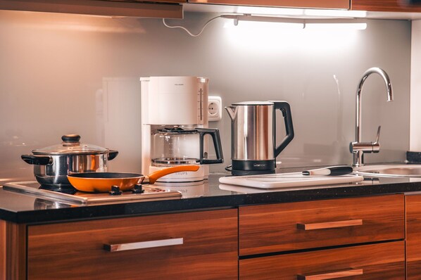 A modern kitchen with a stove, coffee maker, kettle, and a sink. - Strandresidenzen Binz (Binz)