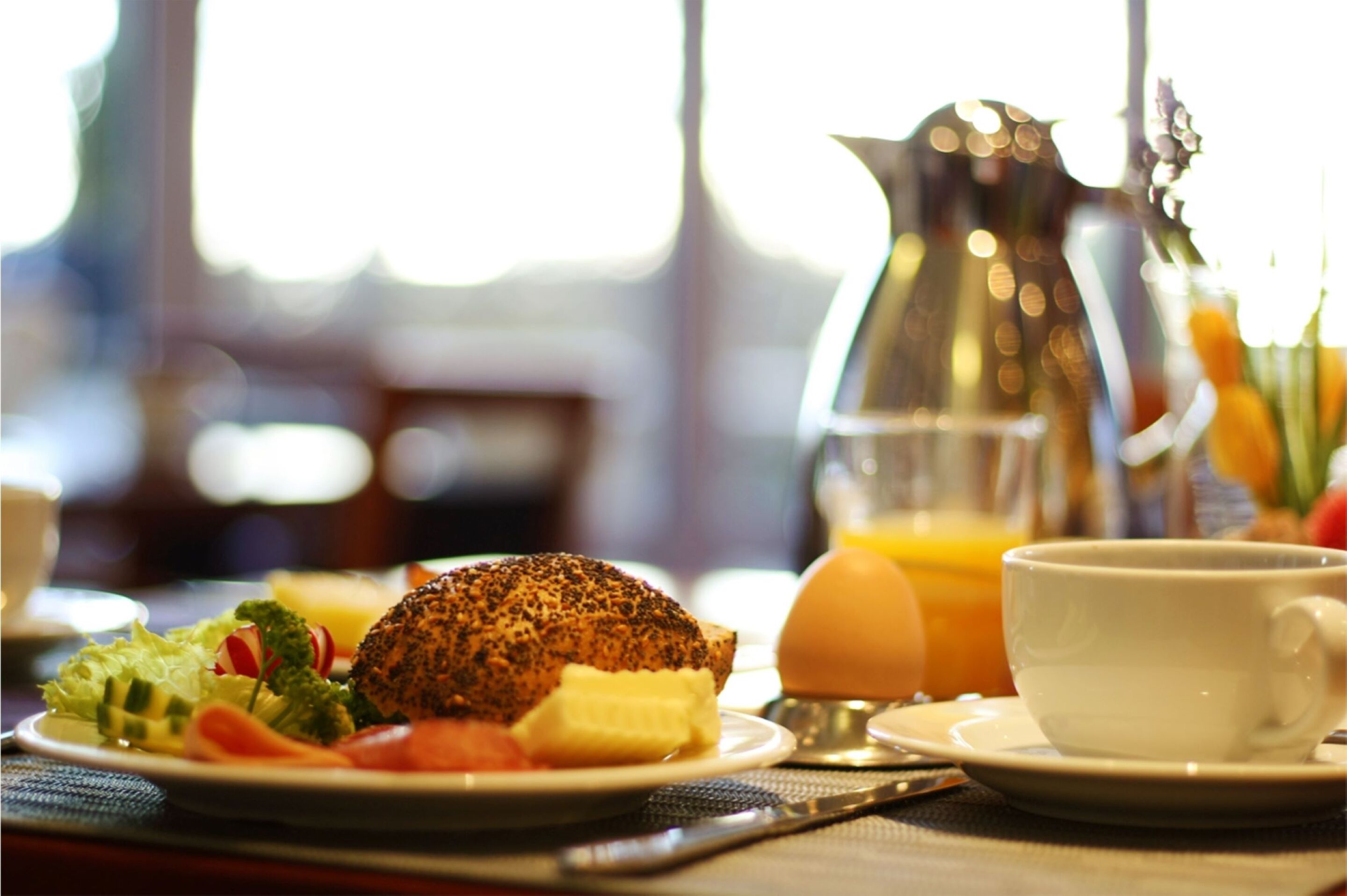 Desayuno con huevos, tostadas, verduras, una taza de café y una jarra de jugo de naranja.