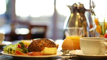 Desayuno con huevos, tostadas, verduras, una taza de café y una jarra de jugo de naranja.