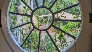 Una ventana redonda con una celosía metálica, rodeada por una pared blanca con detalles oscuros.