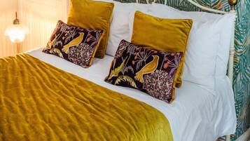 Una cama con cabecera blanca, dos almohadas color mostaza y una colcha verde.