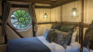 Un dormitorio con ventanal redondo, cama con muchos almohadones y dos lámparas colgantes.