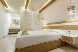 A modern bedroom with a wooden headboard, a bedside table with a vase, and a large mirror. - New Aeolos Hotel (Mykonos)