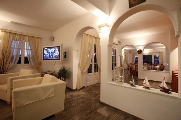 A living room with a television, sofas, and a window with curtains. - New Aeolos Hotel (Mykonos)