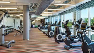 A gym with multiple exercise machines, a patterned carpet, and large windows.