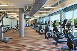 Un gimnasio con varias máquinas de ejercicio, alfombra estampada y amplias ventanas.