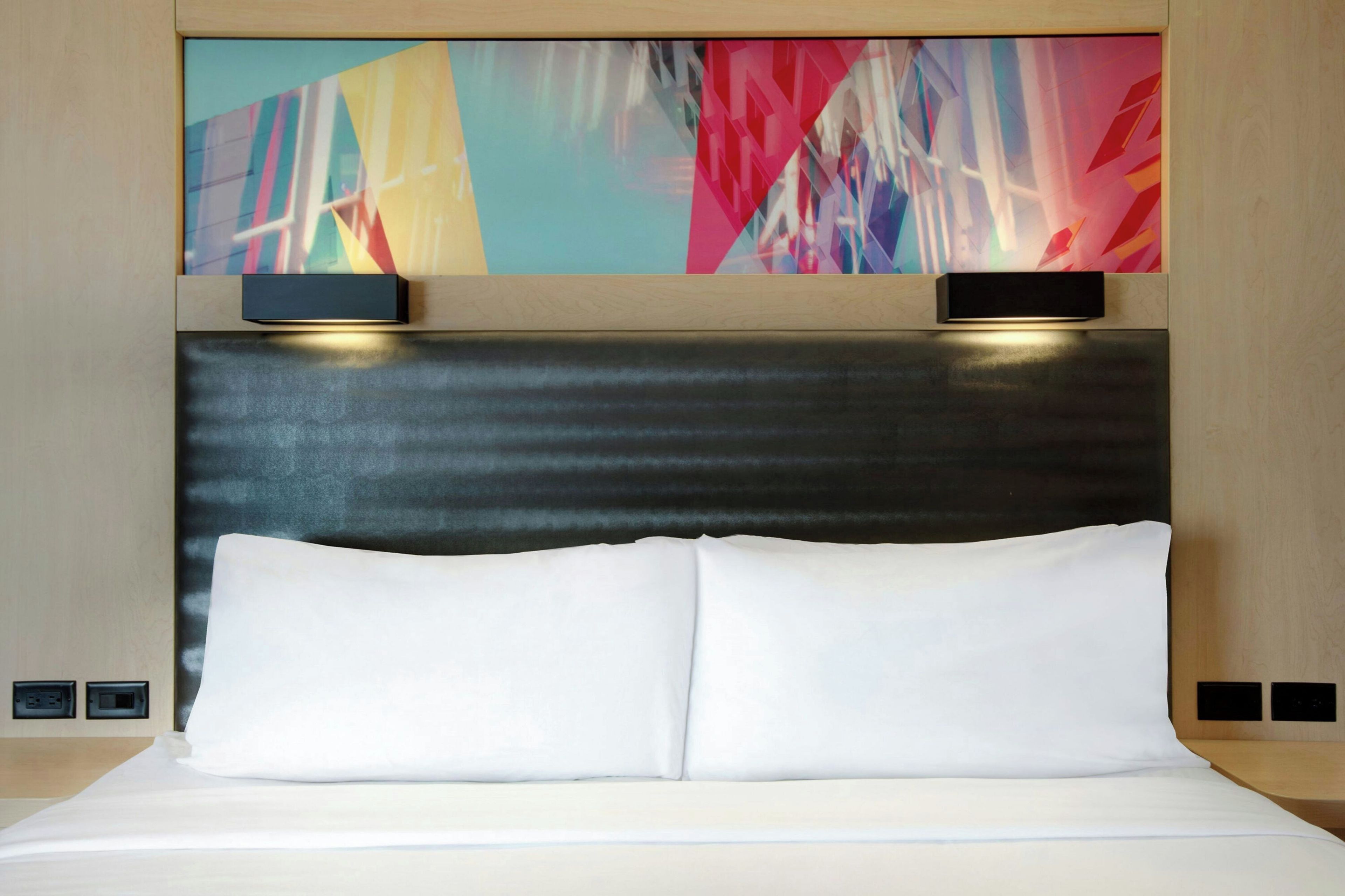 A hotel room with a bed, two bedside tables, a headboard, and abstract wall art.