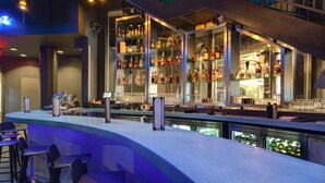 A modern bar area with a curved counter, multiple seating options, and a well-stocked liquor display. - Aloft by Marriott Oklahoma City Downtown - Bricktown (Oklahoma City)