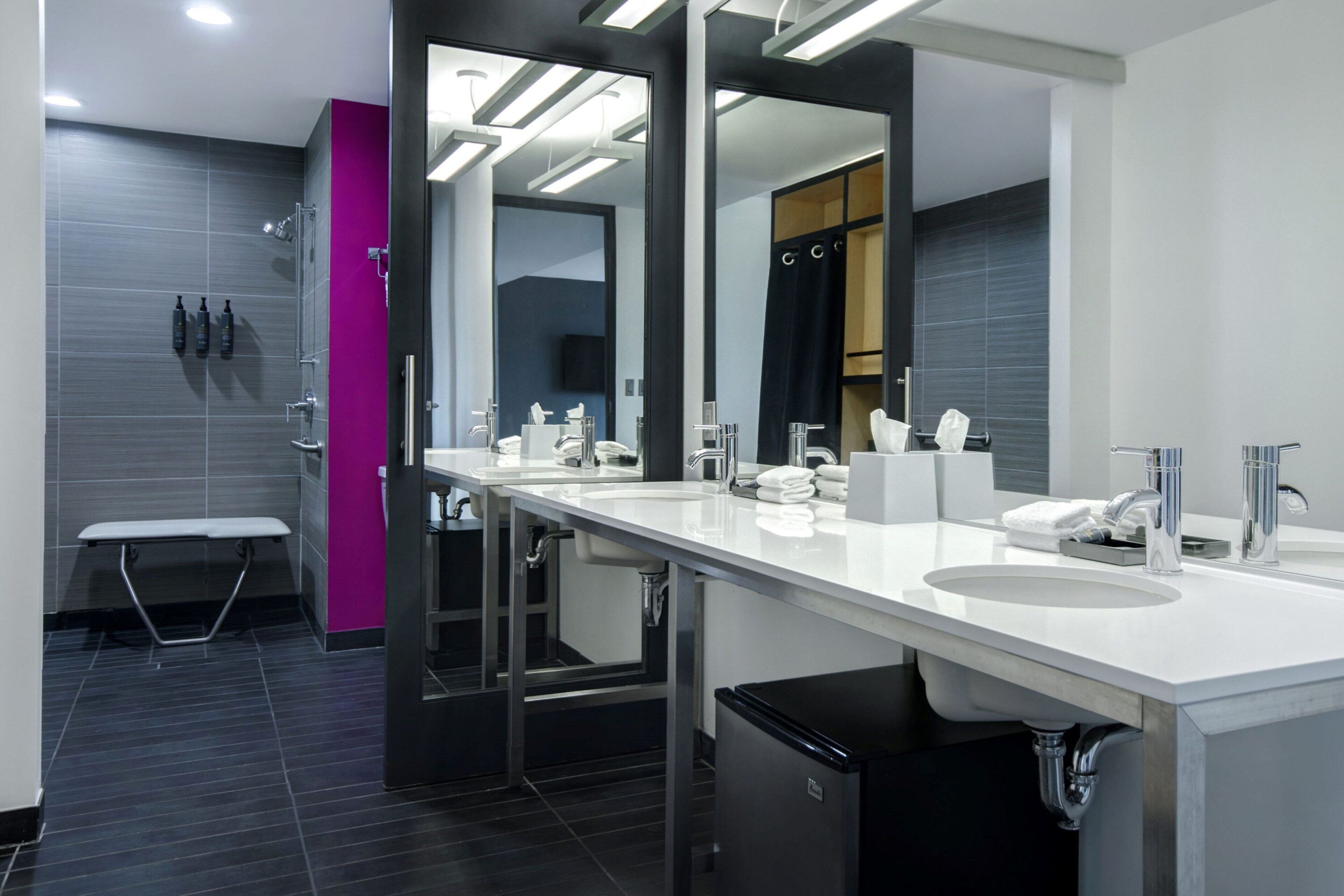 A modern bathroom with dual sinks, a bench, and a mirror.
