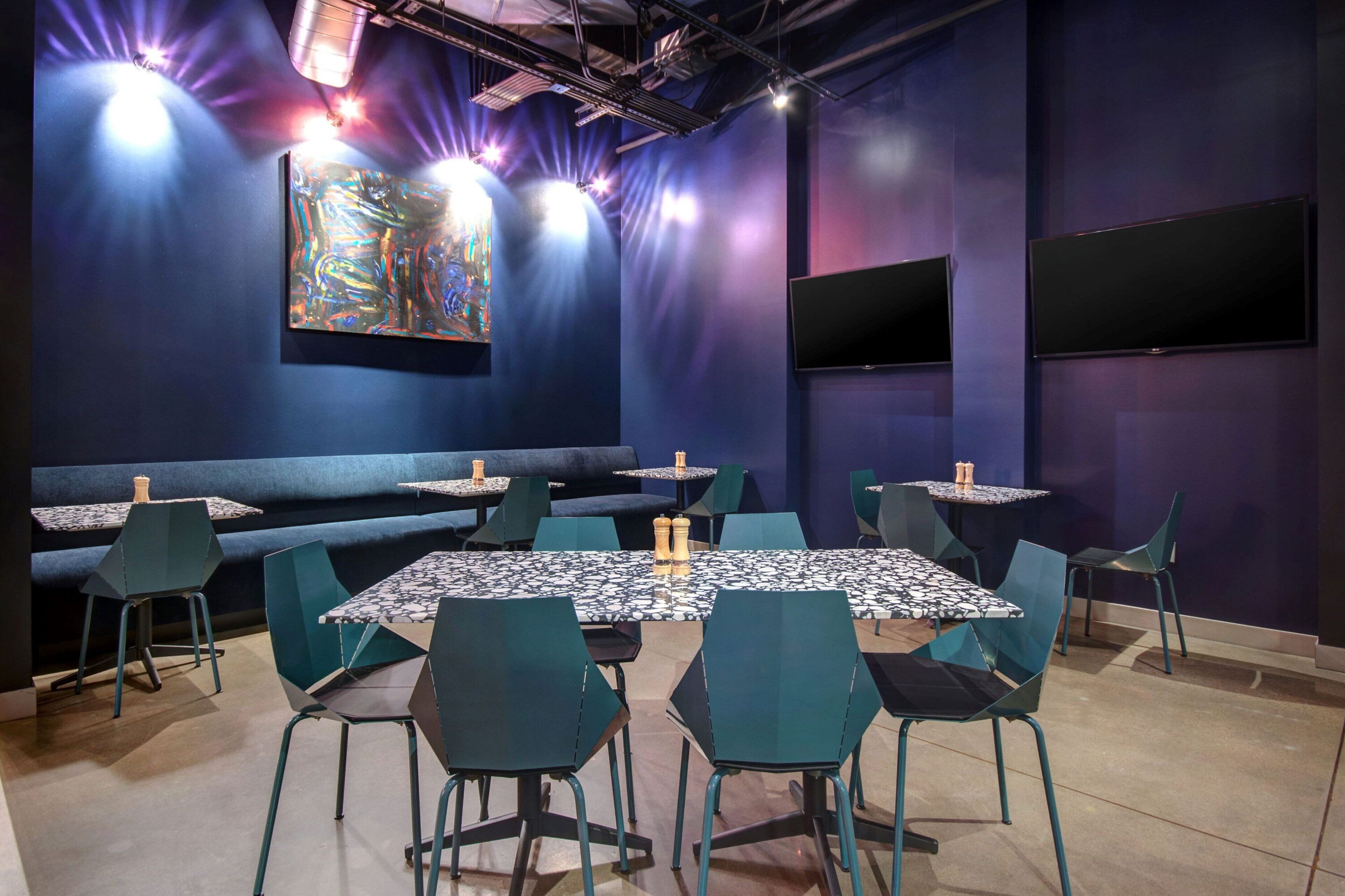 Un restaurante con decoración azul, varias mesas y sillas, y un cuadro abstracto grande en la pared.