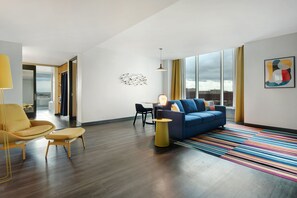 A modern living room with a blue sofa, yellow armchair, and a colorful striped rug. - Aloft by Marriott Oklahoma City Downtown - Bricktown (Oklahoma City)